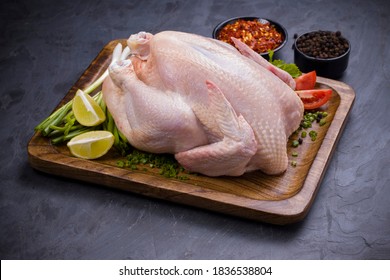 Raw whole chicken with skin arranged on wooden board and garnished with parsely,small tomato,spring onion,chilli flakes and lemon slices with stone textured colour as background ,isolated