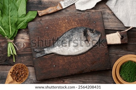 Similar – Image, Stock Photo Raw whole dorado fish on wooden kitchen board and spices for cooking, top view on black table
