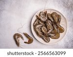 Raw whole fresh uncooked prawns or shrimps in a white plate on a white background. Top view with copy space.