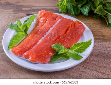 Raw wild king Salmon Fillet lying on white place, on wooden background, decorated with mint leaves and a bunch of mint in the back
