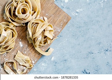 Raw yellow homemade italian pasta pappardelle, fettuccine or tagliatelle on a blue background, close up. Egg homemade noodles cooking process, long rolled macaroni, uncooked spaghetti . - Powered by Shutterstock