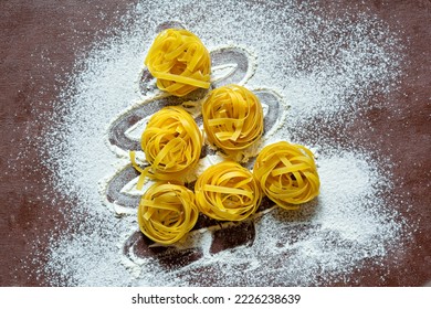 Raw yellow italian pasta (nests) pappardelle, fettuccine or tagliatelle in the shape of a Christmas tree on a brown background, close up. Egg homemade noodles cooking process,festive mood. - Powered by Shutterstock