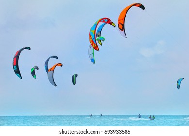 RAYONG, THAILAND - AUGUST 6, 2017 : Group Of Colorful Kites Of Kiteboarding Is Flying In The Blue Sky By The Wind Blow. Player Surfing On The Sea