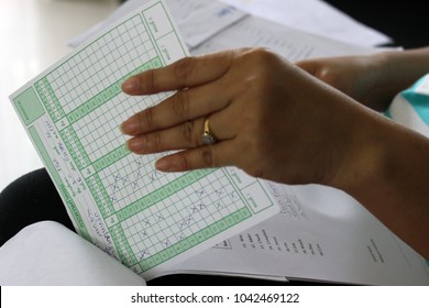 Rayong, Thailand - March 10th, 2018: Close Up Detail Of A Teacher's Hand Grading A Bundle Of School Student Exam Papers And Answer Sheets At The End Of Term.