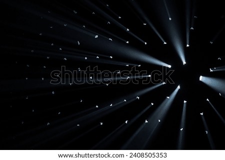 Rays of bright light come through holes in the black background of the studio. The rays cut through the darkness illuminating the space.