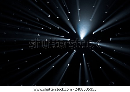 Rays of bright light come through holes in the black background of the studio. The rays cut through the darkness illuminating the space.