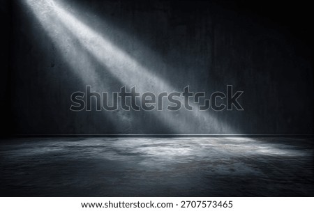 Rays of light shine on a dark grunge wall and concrete floor in an empty interior space.