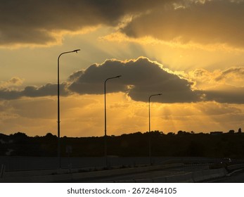 Rays of Light Through Clouds at Sunset
Description: The stunning silhouette of a road and streetlights against a vibrant sky, as the setting sun's rays break through dramatic, dark clouds. The golden 