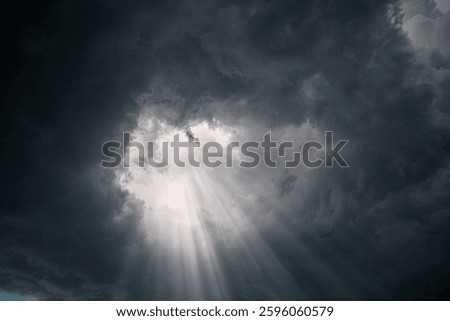 Rays of light through the hole in the dark stormy clouds in the sky.