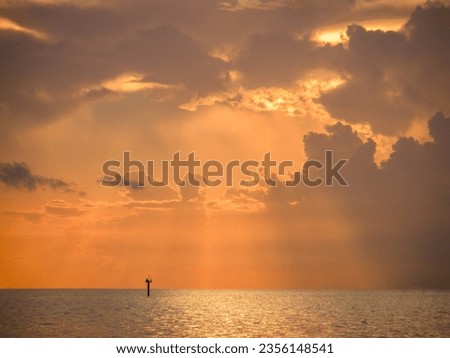 Rays of lights from the setting sun shine on a lonely channel marker in an empty ocean.