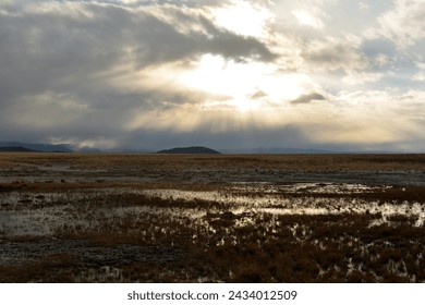 The rays of the setting sun break through the clouds of a storm front over the swampy steppe in early autumn. Chui steppe, Altai, Siberia, Russia.