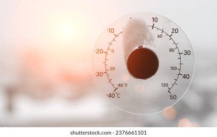The rays of the setting sun in the sky against the background of a street thermometer with a snow cap on the window. Snowy weather and warming concept. Weather forecast