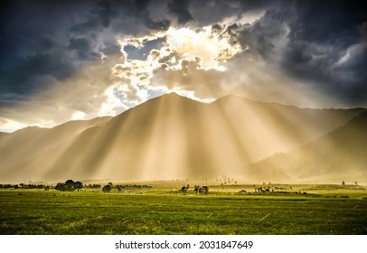 The rays of the sun from behind the clouds illuminate the valley. Sunrays from sky clouds. Cloudy sky sunrays. Beautiful sunrays from cloudy sky