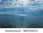 Rays of sun shining through the clouds in blue sky over the sea.