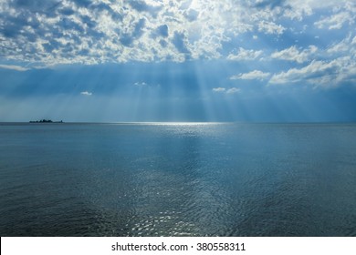 Rays of sun shining through the clouds in blue sky over the sea.