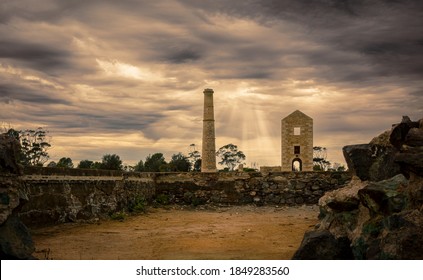 Rays of sunlight breaking through storm clouds behind an the ruins of a Cornish Enginehouse and old mine buildings.