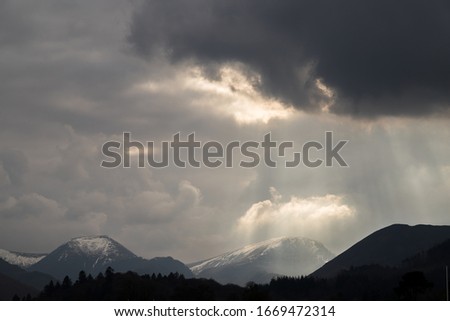 Rays of sunlight peak through the clouds and light up the snowy mountain tops around Derwent Water.