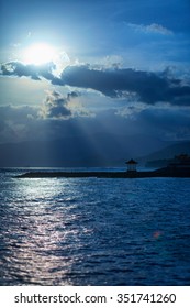 Rays of sunshine beam down through the clouds over a seaside pagoda on a picturesque tropical beach.