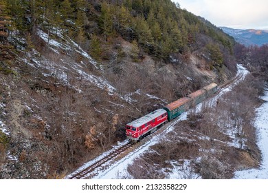 Razlog, Bulgaria - Winter 2022: Red Locomotive Pulls A Commuter Passenger Train Along A Winding Road Among High Mountains. Suburban Railway Transportation. Bulgarian Railways