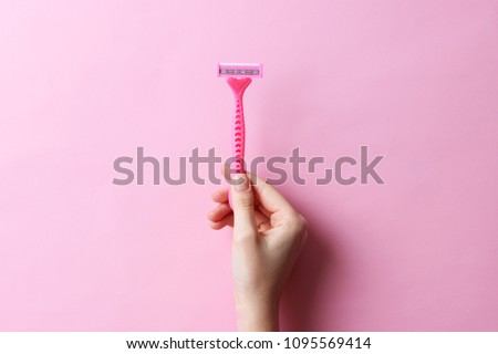 razor in a female hand on a colored background. Removal of unwanted hair. minimalism, the top
