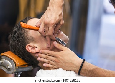 Razor In Hands Of Specialist Barber. Barber Shaving A Man In A Barber Shop, Close-up. Man Mith Mustaches Having A Shave