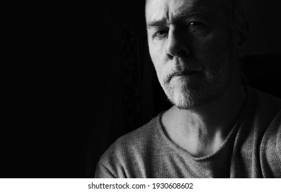 RCT, UK, March 6th 2021 : tough-looking middle aged man with stubble wearing t-shirt staring coldly with dark black background.