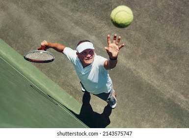 Reach for the sky. High angle shot of a focused middle aged man playing tennis while about to serve the ball to his opponent outside during the day. - Powered by Shutterstock