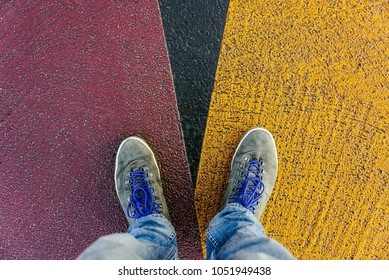 Reaching A Crossroads Having To Decide About Past, Now And Future Symbolized By Two Feet And Shoes Standing On Two Different Colors On Pathway From Above