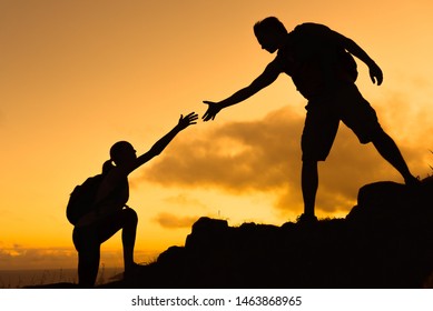 Reaching Out For Help. Man Giving His Hand Helping Female Hiking Partner Up A Mounting. Teamwork, Courage, And Determination Concept. 