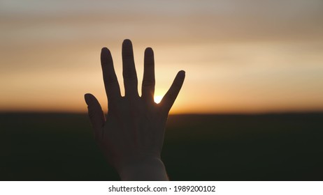 Reaching out to the sun, happy girl at sunset, sunlight shining on her hand, solar system star, happy family concept, touching a dream, asking for help from God, natural phenomenon