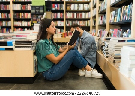 Readers sitting on the floor at the bookstore and reading a fiction novel together while shopping