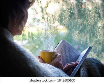 Reading a book with a cup of hot tea on a rainy day.