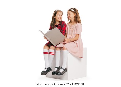 Reading Book. Studio Shot Of Little Happy Girls In Retro Style Outfit, Fashion Of 70s, 80s Years Isolated On White Background. Concept Of Emotions, Facial Expression, Beauty. Copy Space For Ad