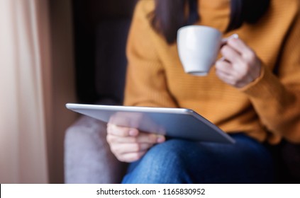 Reading Concept. Young Woman Using Tablet  And Drinking Coffee. Relaxing In Cozy House, Sit On The Chair, Front View And Selective Focus