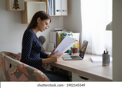 Reading contract. Focused millennial woman in glasses work with paper document hardcopy. Concentrated female remote employee engaged in studying terms conditions of loan agreement by home office desk
