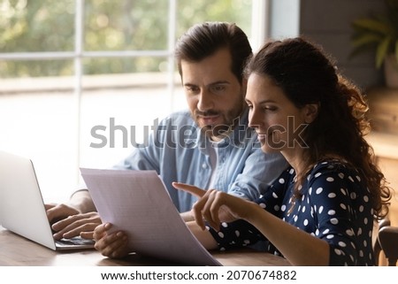 Reading documents. Family couple study papers search information by loan mortgage affordable housing program on website. Young spouses clients hold bank account statement check financial data online