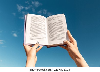 reading, education and knowledge concept - close up of hands holding open book over blue sky - Powered by Shutterstock