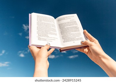 reading, education and knowledge concept - close up of hands holding open book over blue sky