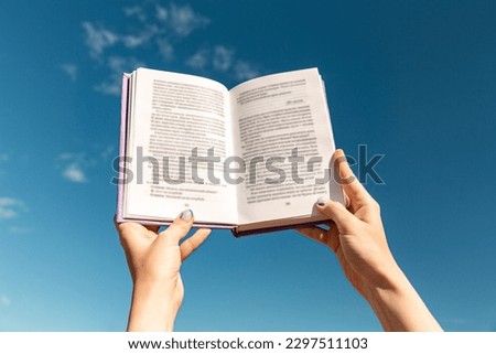 reading, education and knowledge concept - close up of hands holding open book over blue sky