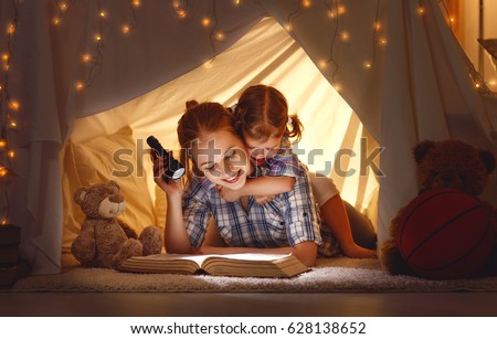 reading and family games in children's tent. mother and child daughter with  book and flashlight before going to bed