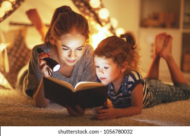 Reading And Family Games In   Tent. Mother And Child Daughter Reading Book And Flashlight Before Going To Bed
