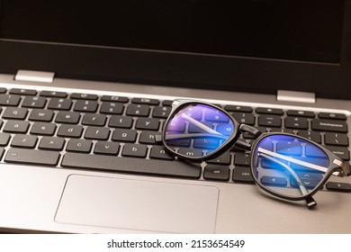 Reading glasses with coating filter to prevent Computer Vision Syndrome (CVS) sit on laptop keyboard. Concept of digital eye strain caused by screens and monitors of smartphones and computer devices. - Shutterstock ID 2153654549