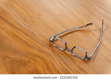 Reading glasses lie on a smooth wooden surface, bathed in natural light, suggesting a quiet moment in a comfortable indoor environment. - Powered by Shutterstock