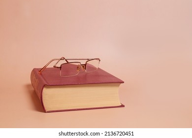 Reading Glasses Lie On A Thick Book, Colored Background. Side View, Space For Text