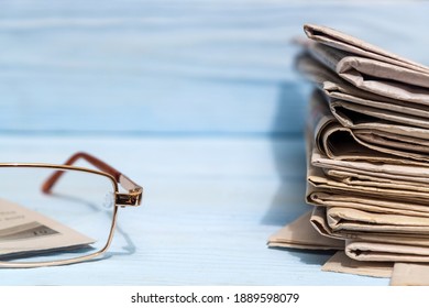 Reading glasses and stack of newspapers on blue wooden shelf