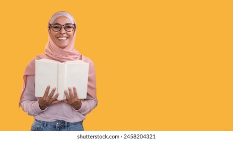 Reading hobby. Learning wisdom. Smart happy smiling woman in headscarf glasses with open book isolated on orange empty space background. - Powered by Shutterstock