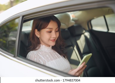 Reading Information From Smartphone. Smart Businesswoman Sits At Backseat Of The Luxury Car With Black Interior.