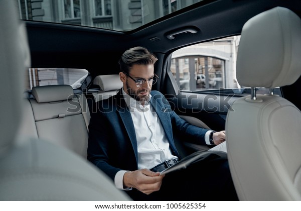 Reading latest news. Handsome\
young man in full suit reading a newspaper while sitting in the\
car