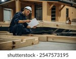 Reading the plan. Male builder is at construction of wooden house.