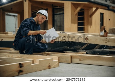 Reading the plan. Male builder is at construction of wooden house.